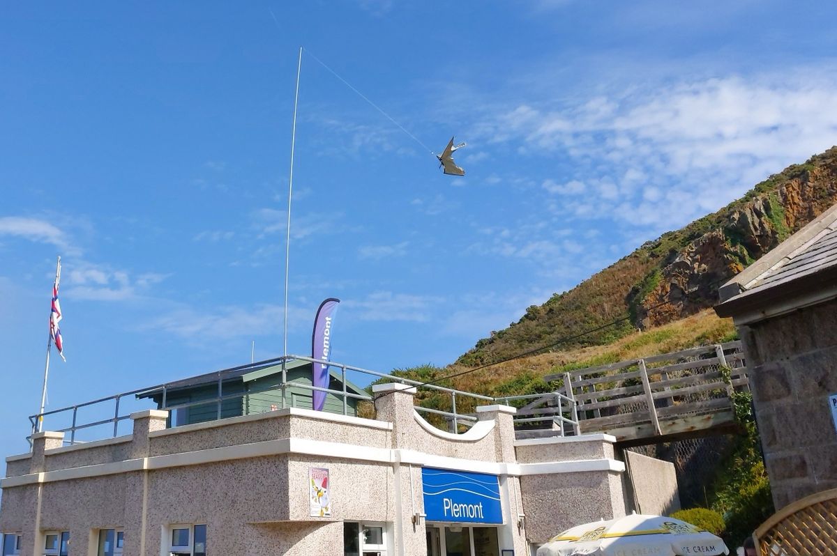 Plémont Beach Café in St Ouen, Jersey, Channel Islands, with the headland behind it under a blue sky.