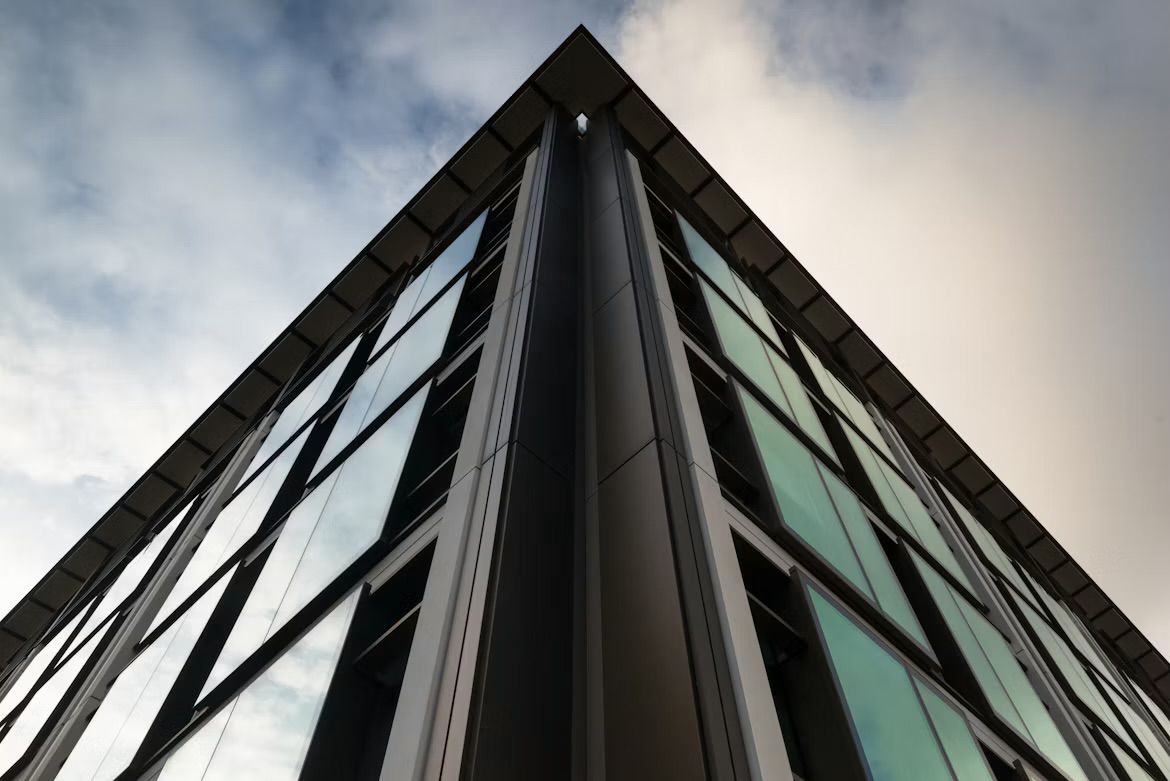 Looking up at the corner of a glass office building in St Helier, Jersey, Channel Islands, against a cloudy sky.